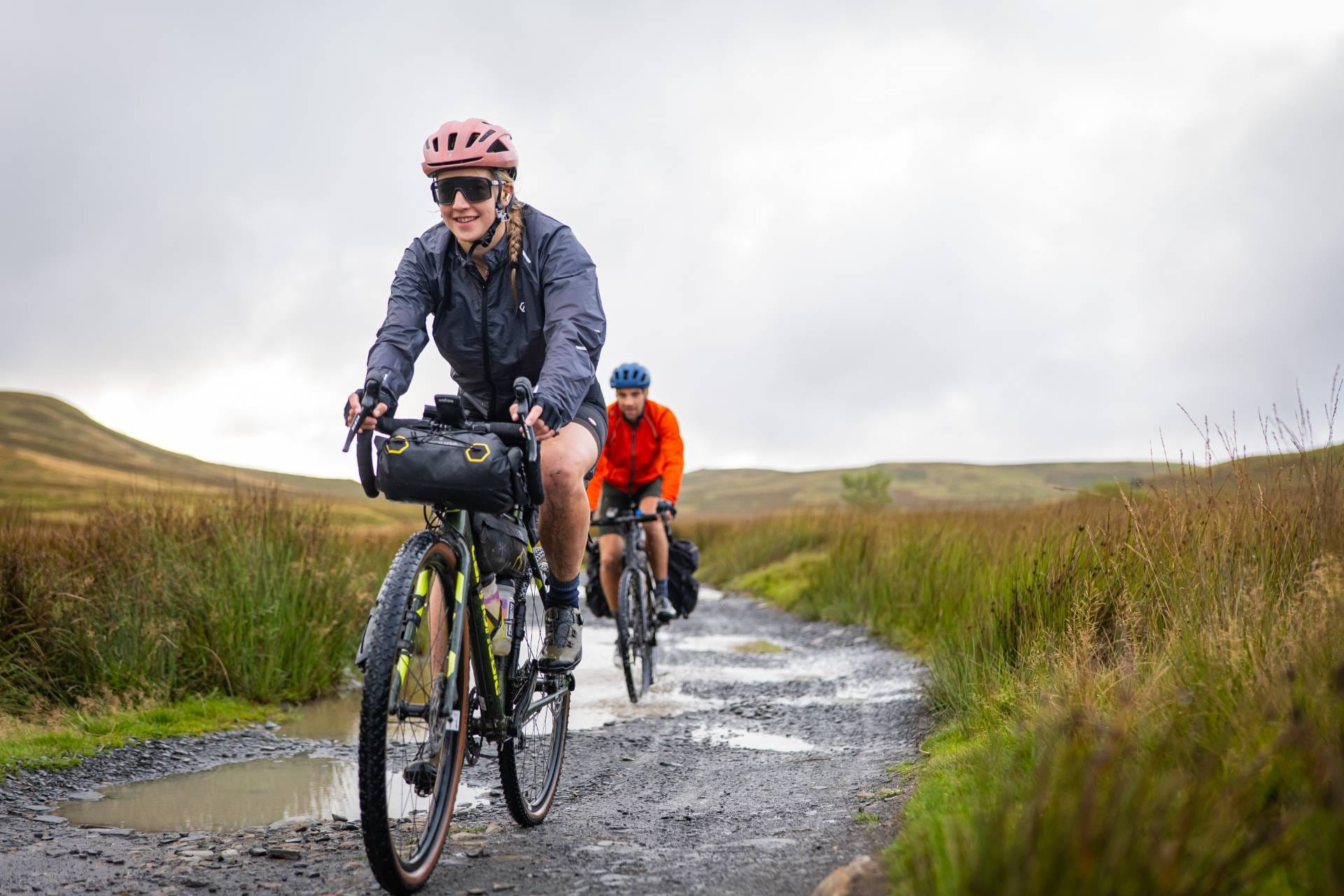 Two riders on a wet gravel track across open moorland