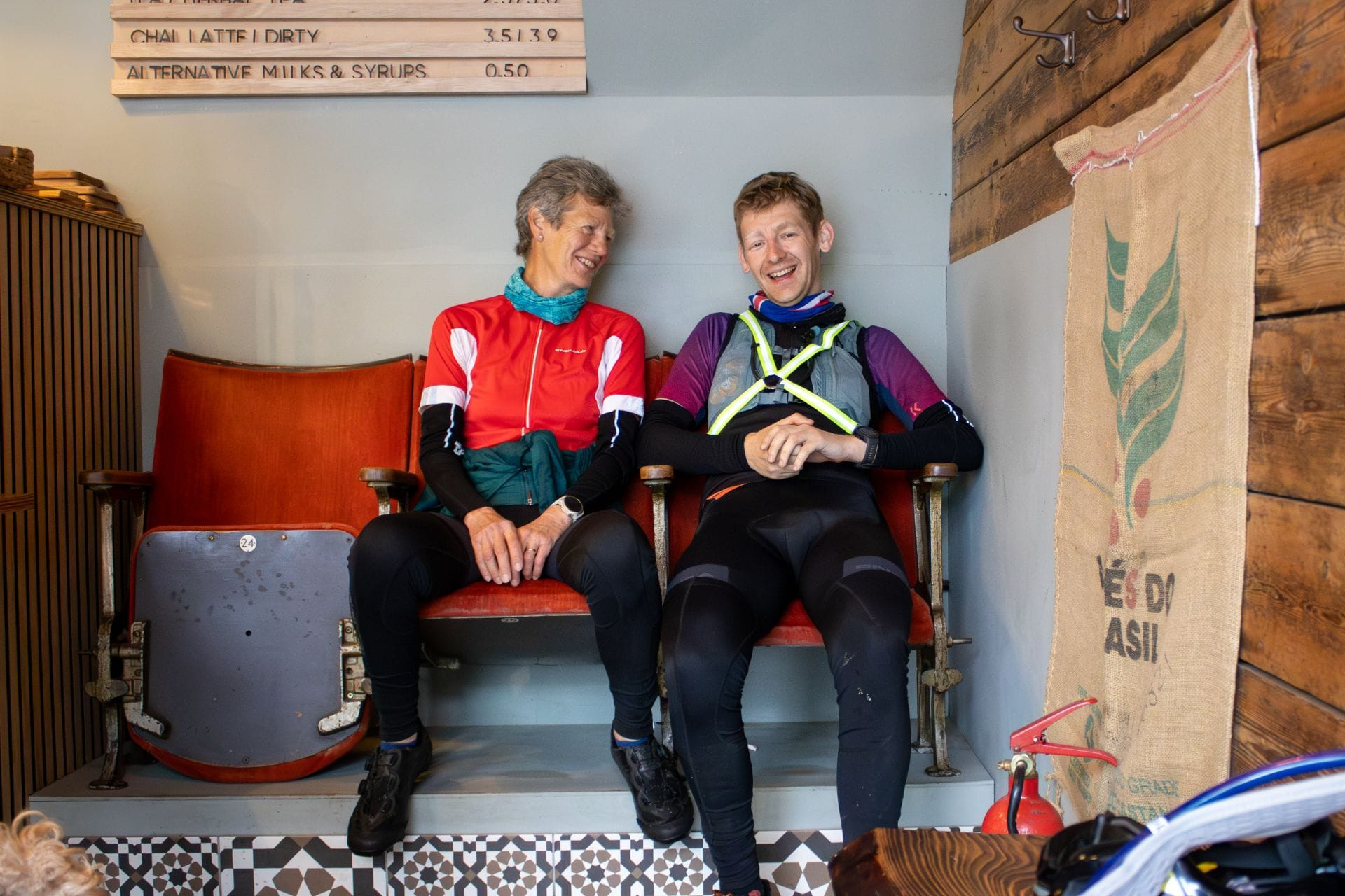 Two riders resting side by side on a bench at the finish