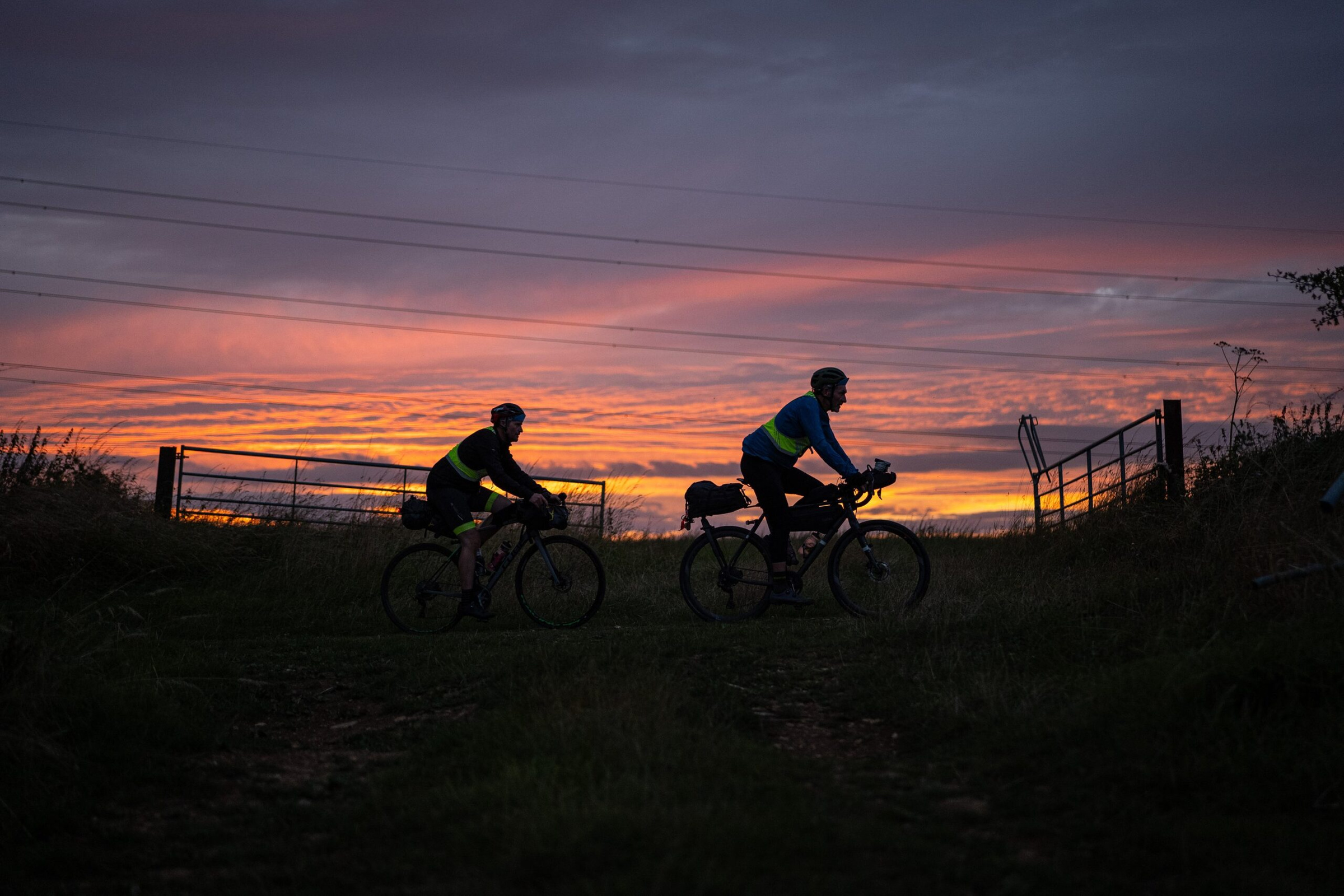 Two riders silhouetted against a sunset at a gate on Cleeve Hill