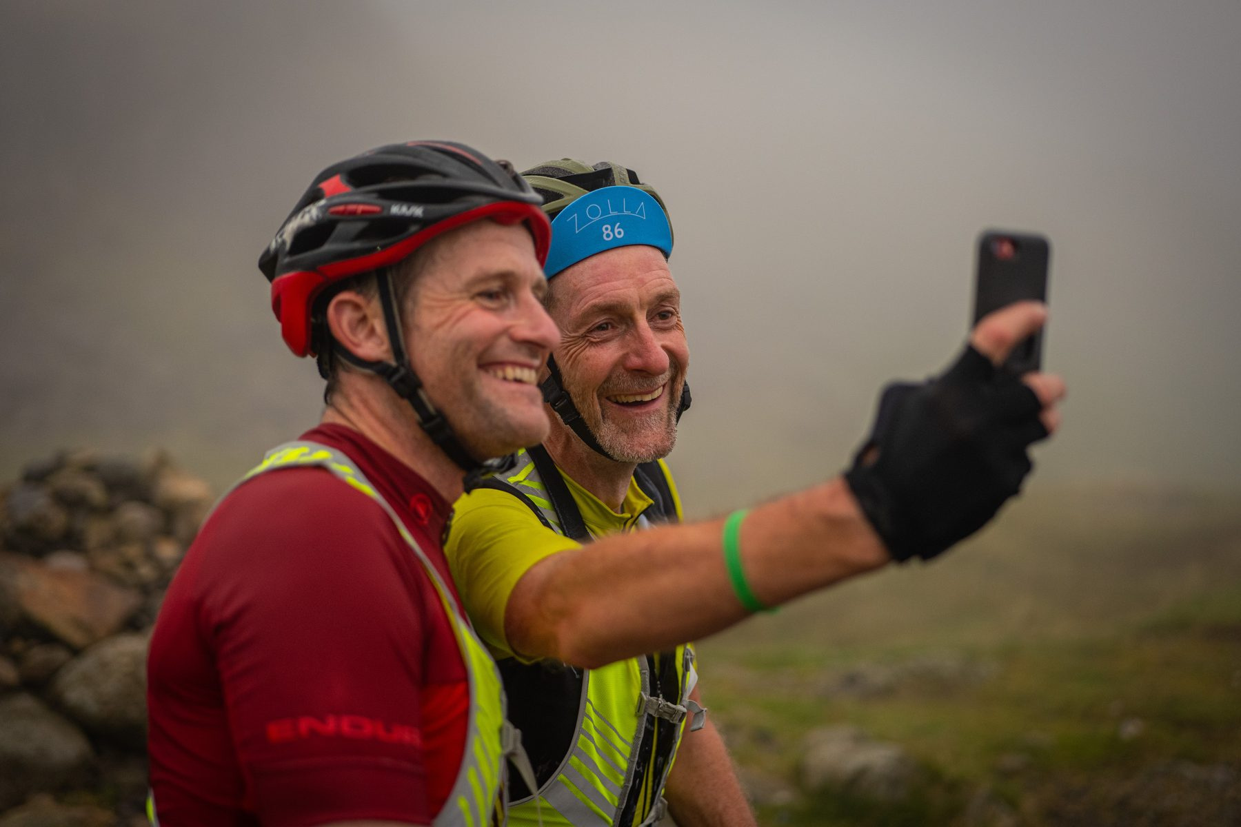 Two riders laughing into a phone selfie in the mist