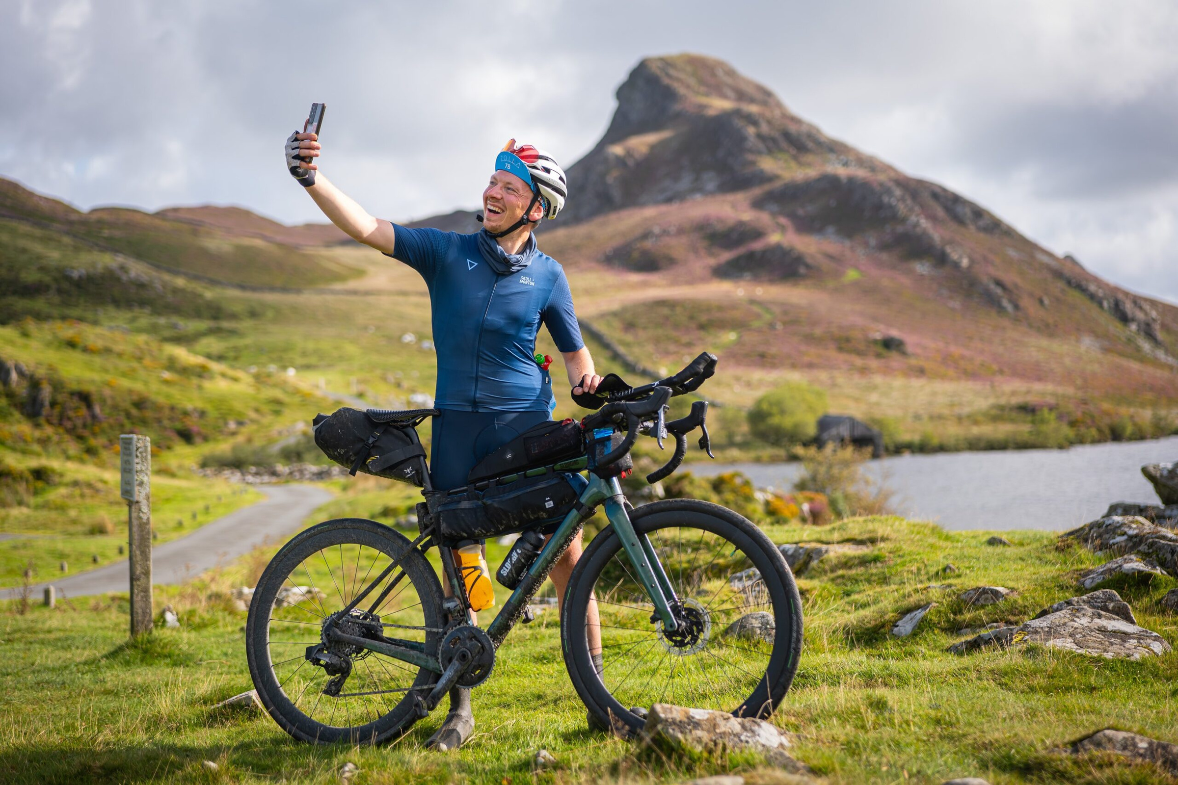 A rider taking a selfie beside his bike beneath a rocky peak at Cregennan Lakes