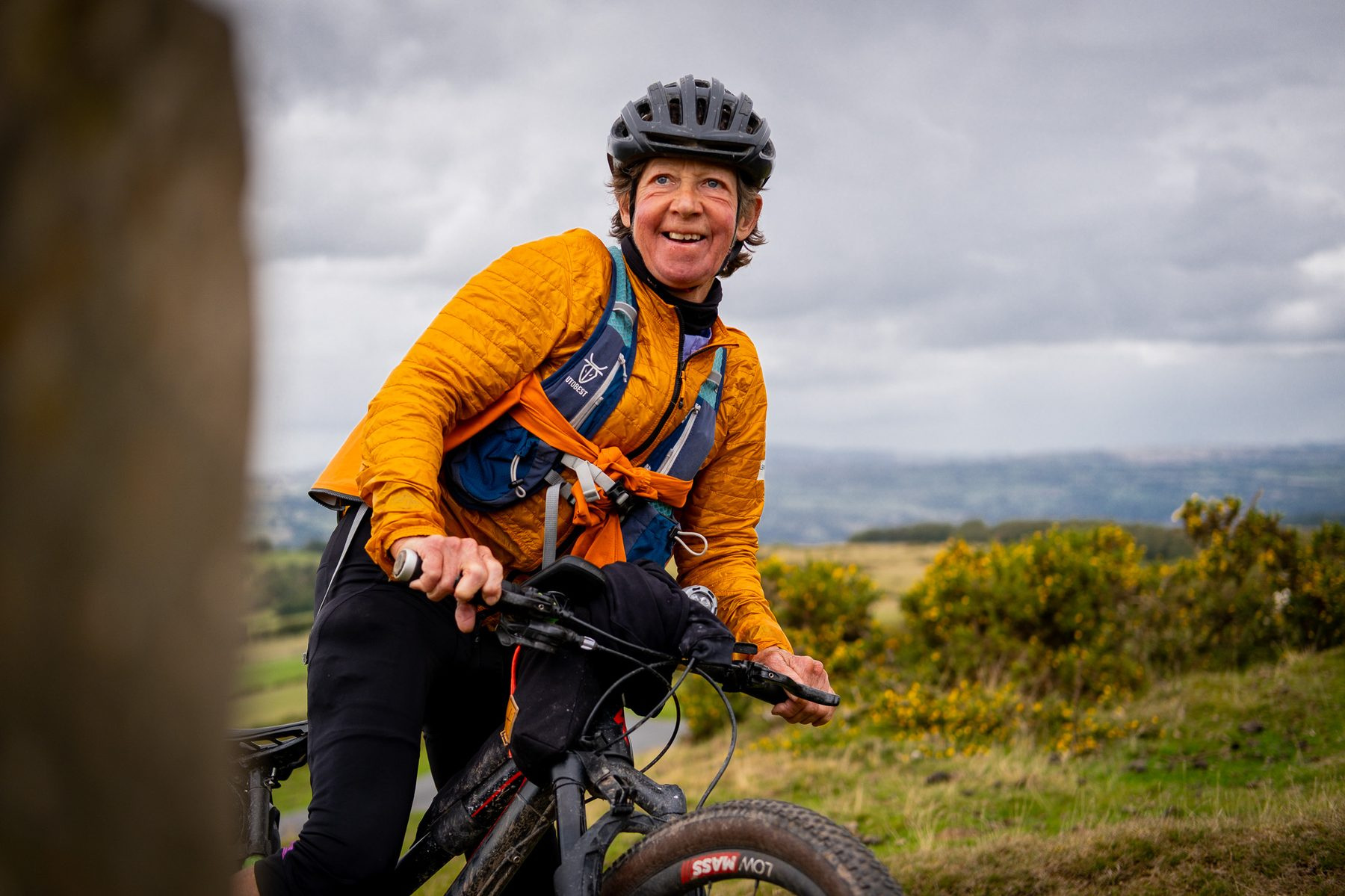 A rider in an orange jacket laughing on a hillside
