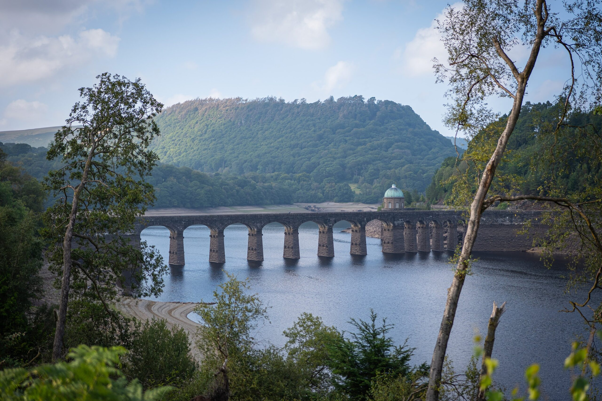 The stone arches of Garreg Ddu viaduct across a reservoir in the Elan Valley, framed by trees