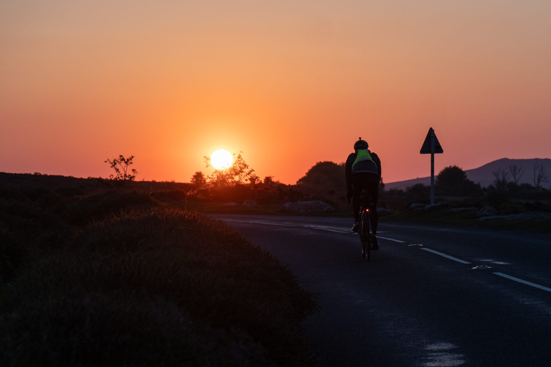 A rider silhouetted against a red sunset on a moorland road